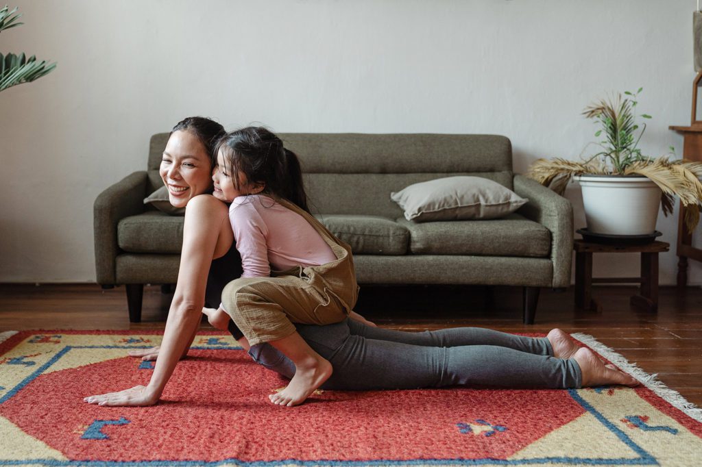 To support mental health, a mother does upward dog yoga pose with her daughter on her back