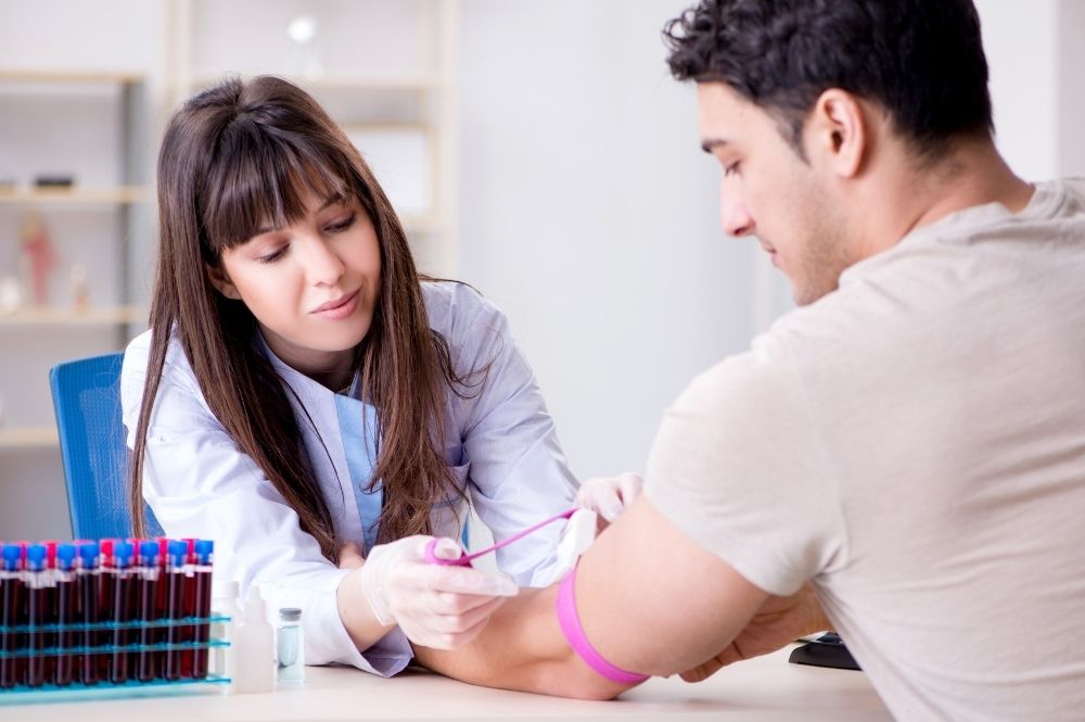 A female phlebotomist administers a blood test to a male patient.