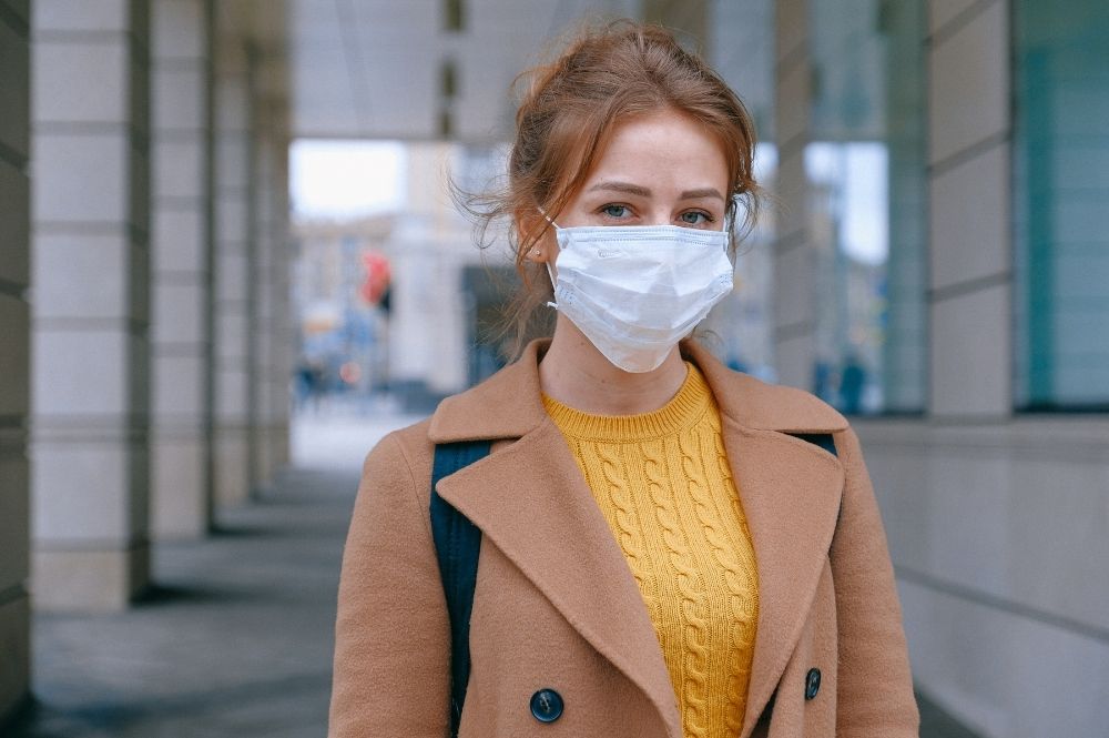 A young woman stands outside wearing a mask to protect against the COVID 19 Delta variant.